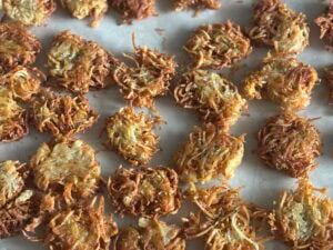 A close-up of several golden-brown potato latkes arranged on a sheet of parchment paper, highlighting the crispy, shredded texture of these classic potato latkes.