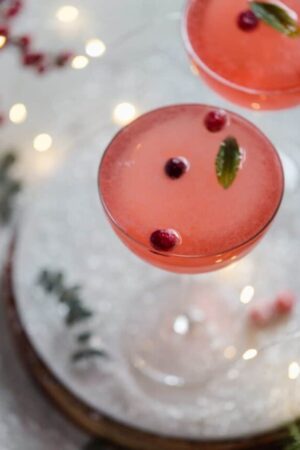 Cranberry gin cocktail in a coupe glass with sugared cranberries and mint garnishes.