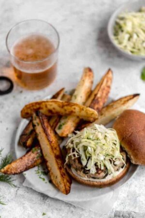 Turkey burger on a plate with coleslaw on top next to potato fries.