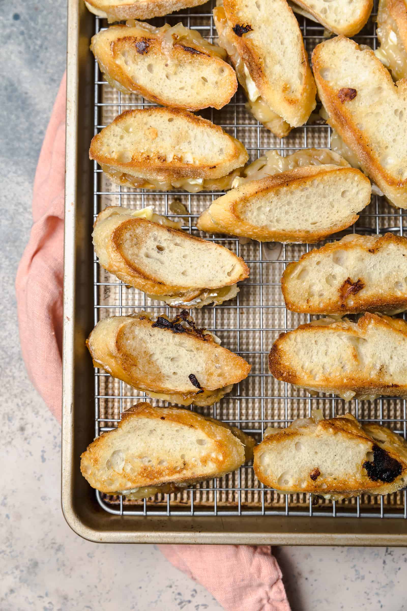 Mini grilled cheese sandwiches with brie and onions on a wire rack set on a baking sheet after griddling.