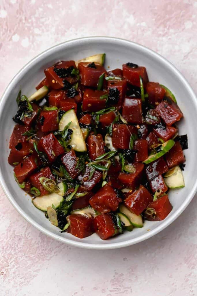Marinated ahi tuna poké with avocado, scallions, crumbled seaweed, and cucumbers in a bowl.