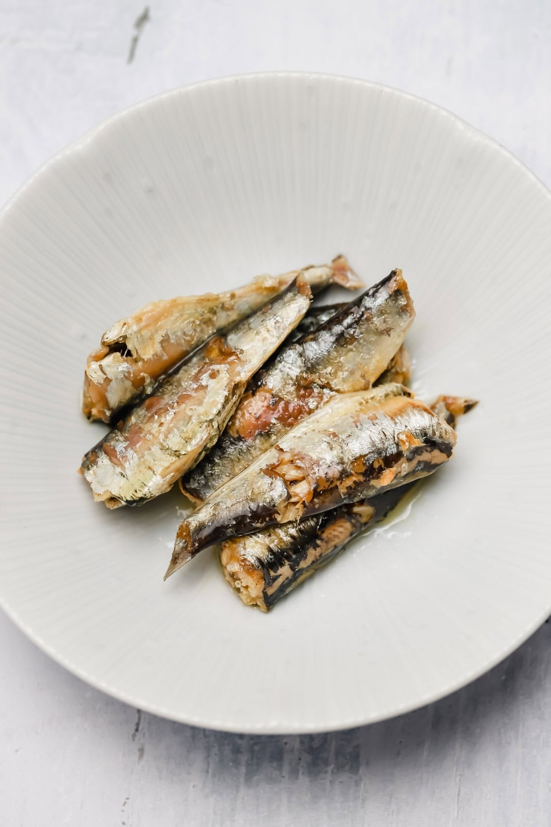 A white plate with several cooked sardines arranged in the center, shown on a light background—a simple yet inviting presentation, perfect for preparing delicious sardine rillettes.