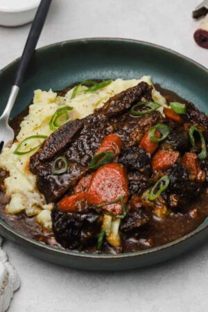 Flanken ribs with prunes and carrots on a plate with mashed potatoes.