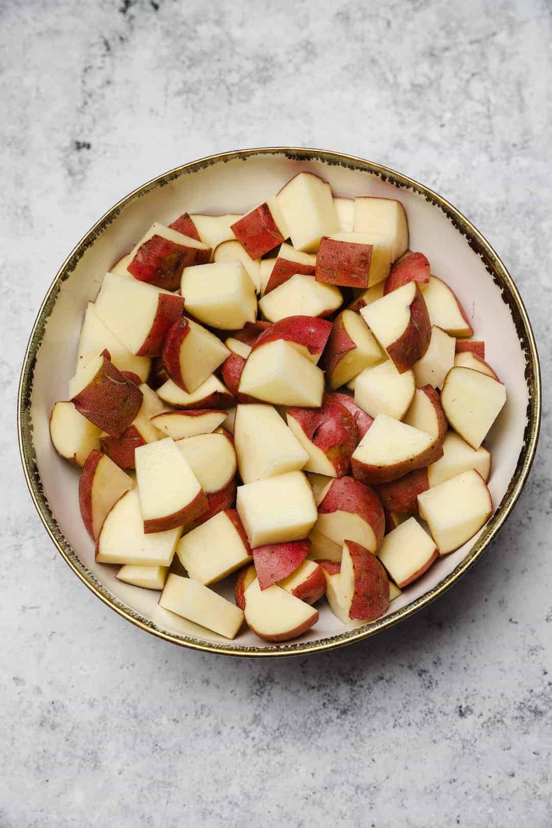 Unpeeled red potatoes cut into 2-inch chunks in a bowl.