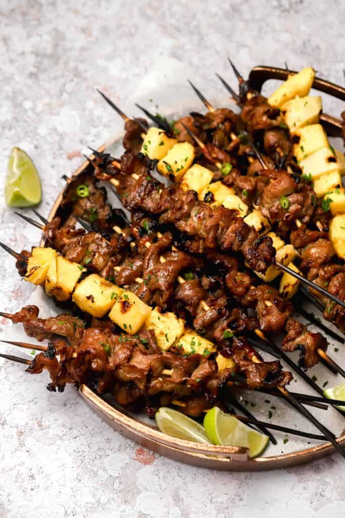 Pork skewers with pineapple on a tray with lime wedges.