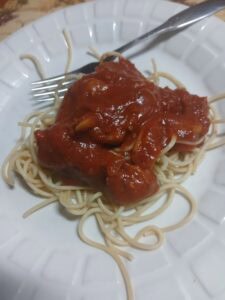 A white plate with a serving of spaghetti topped with tomato sauce, mushrooms, and savory sausage ragu, with a fork resting on the edge of the plate.