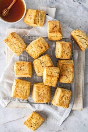 Cheddar biscuits with black pepper on a cooling rack with honey in a small bowl to the side.