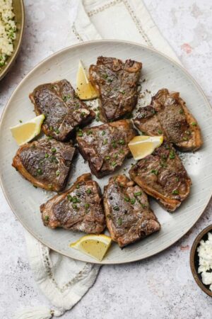 Sous vide lamb chops with garlic and lemon wedges on a plate.