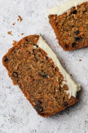 Slice of carrot cake loaf with raisins and cream cheese frosting.