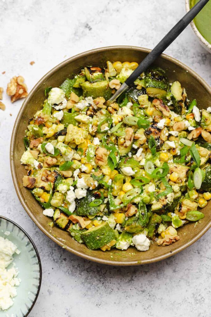 Grilled corn salad in a bowl with a black spoon and feta cheese on top.