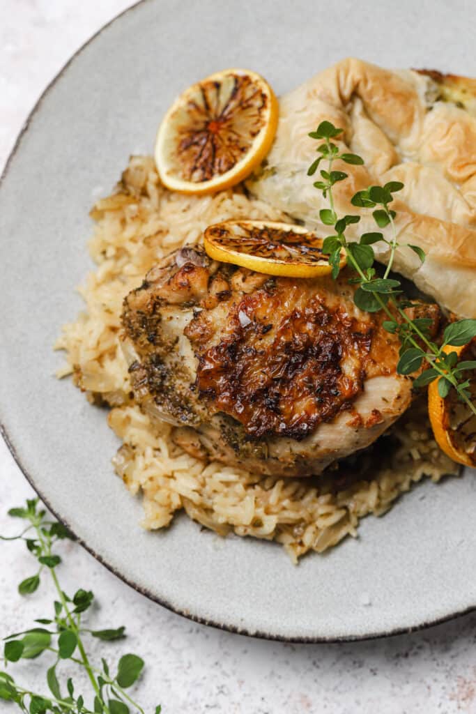 Greek style chicken thighs with rice on a plate.