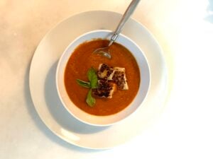 Roasted tomato soup in a bowl with fresh basil and grilled cheese croutons.
