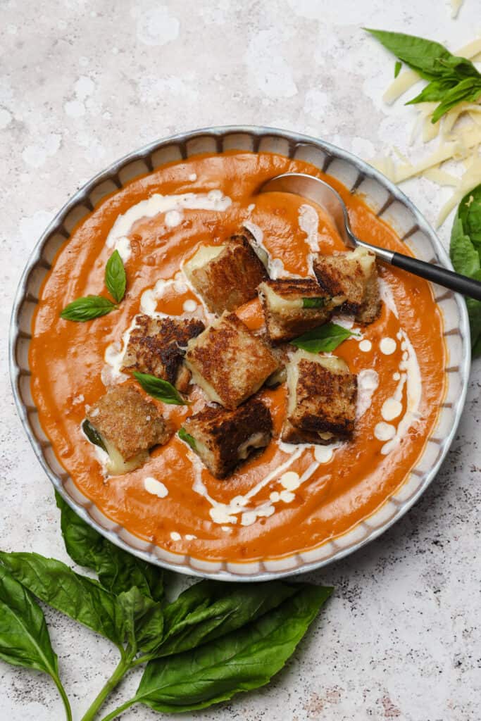 Roasted tomato soup with Gruyere grilled cheese in a bowl with heavy cream and basil.