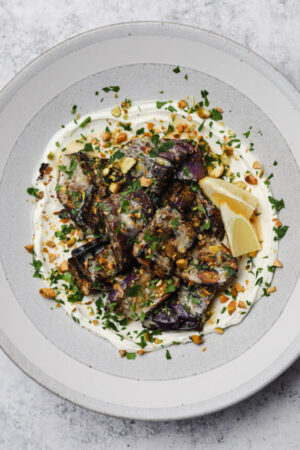 Grilled eggplant skewers on Greek yogurt with tahini drizzled on top.