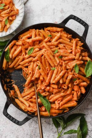 Penne alla vodka in a large skillet with fresh basil leaves.