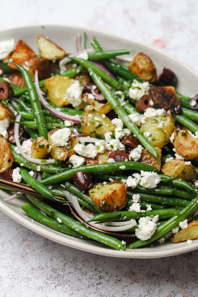 Roasted potato and green bean salad recipe with feta cheese and black olives in a serving bowl.