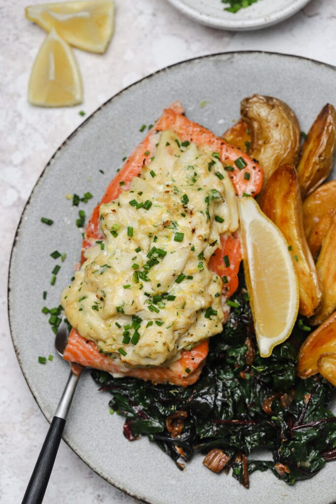 Stuffed baked salmon with crab and cream cheese filling on a plate with potatoes and Swiss chard.