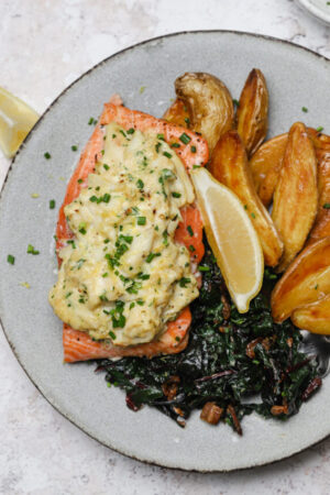 Salmon fillets stuffed with crab filling on a gray plate with roasted fingerling potatoes and sautéed Swiss chard.