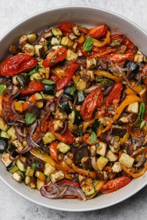 Sheet pan roasted vegetable ratatouille in a bowl with fresh basil.