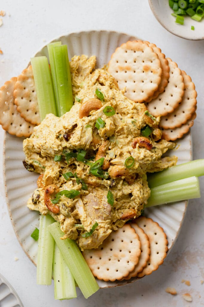 Curried chicken salad on a plate with crackers and celery sticks.