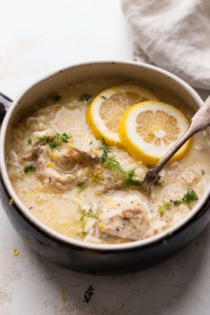 Chicken and rice soup with lemon and fresh herbs in a bowl with a spoon.