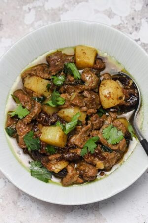 Lamb shoulder braised with curry spices and potatoes in a bowl with fresh cilantro.