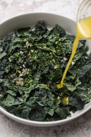 Pouring salad dressing over sliced kale leaves.