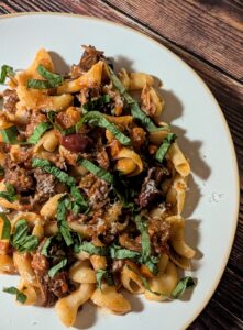 Braised lamb ragu with olives and basil over pasta.