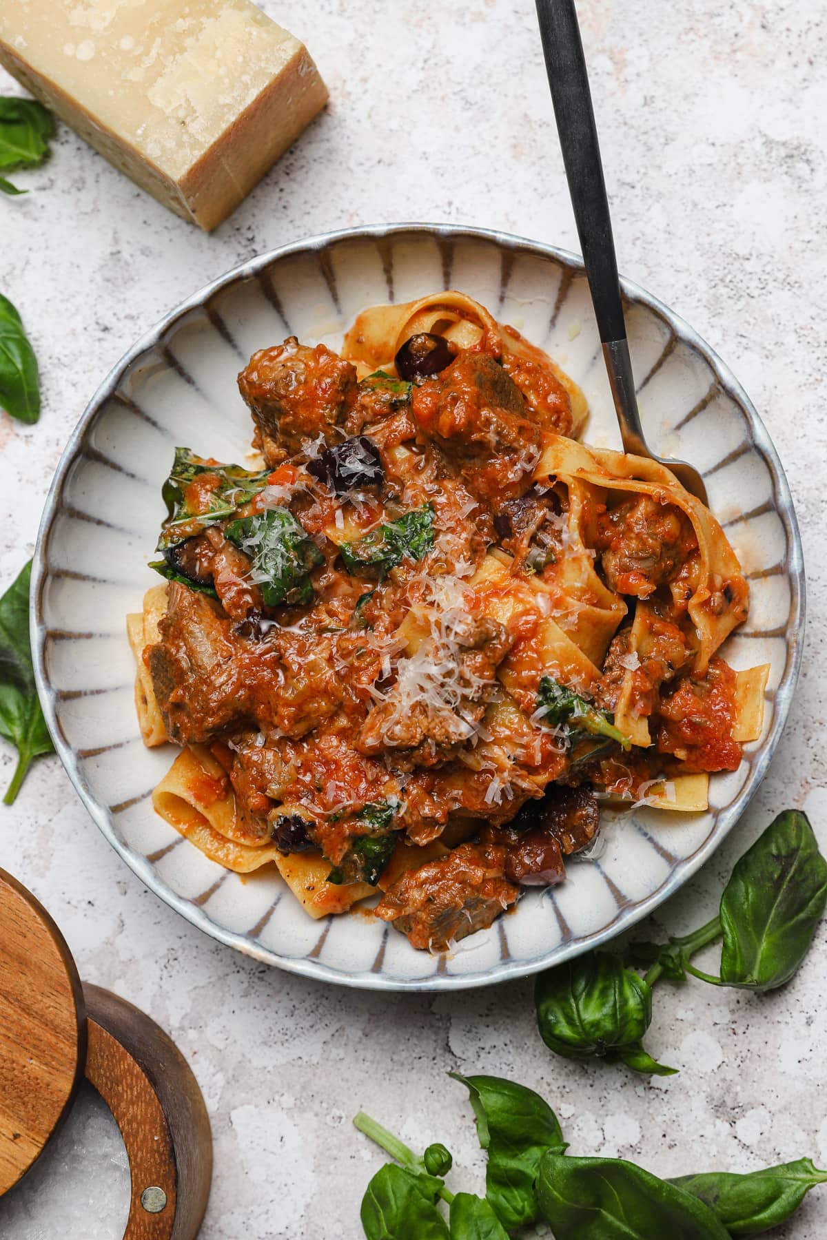 Braised lamb ragu with basil olives and capers in a bowl with fresh pasta.