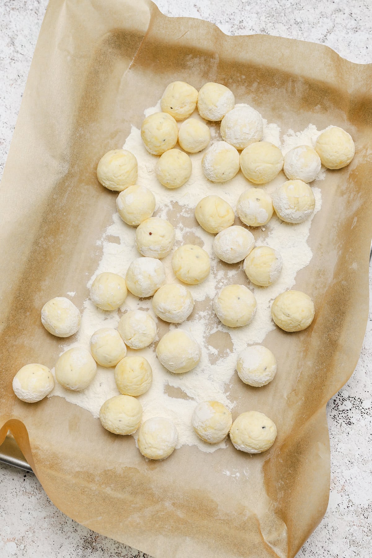 Formed ricotta gnudi on a floured sheet pan with parchment.