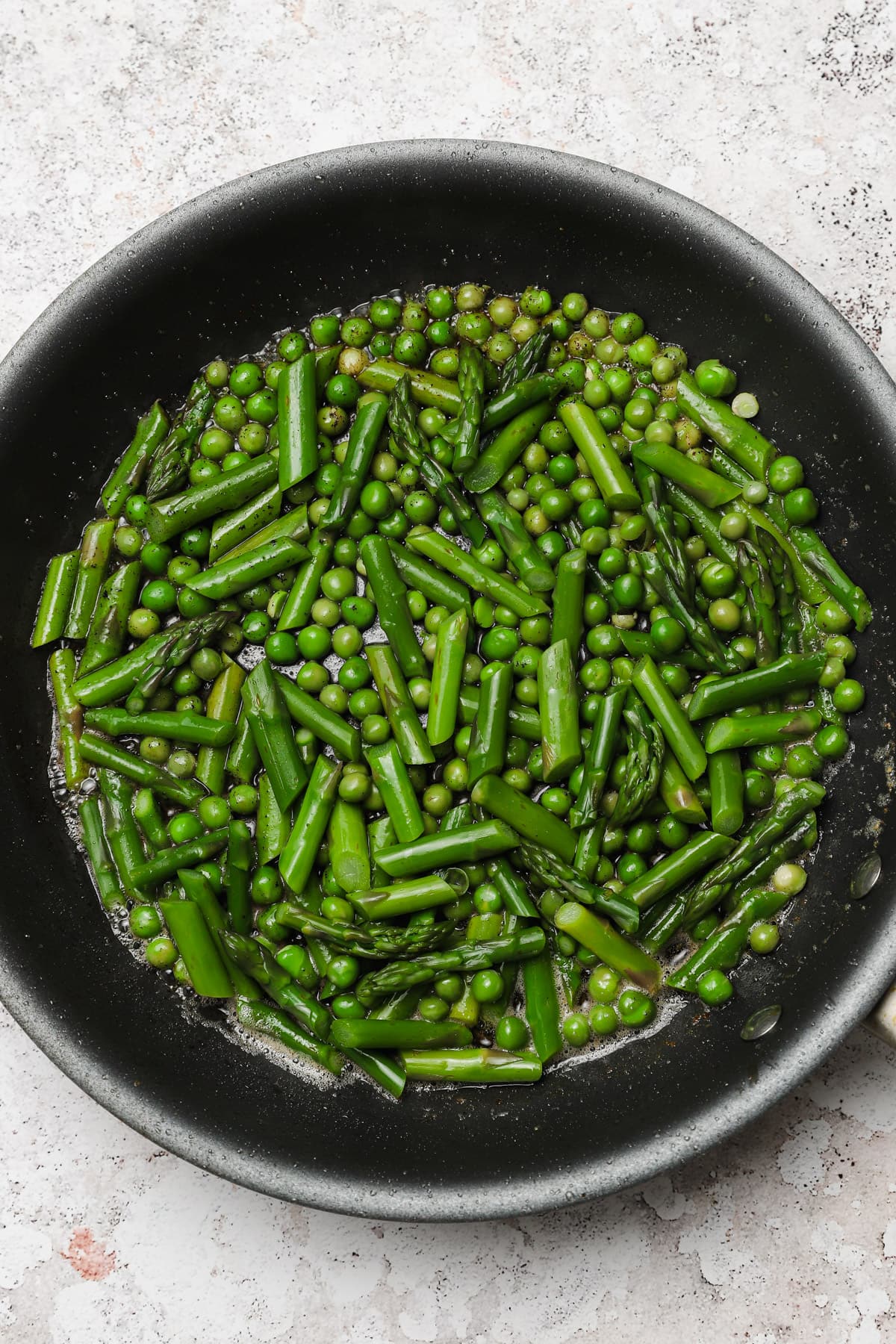 Sautéed peas and asparagus in a skillet.