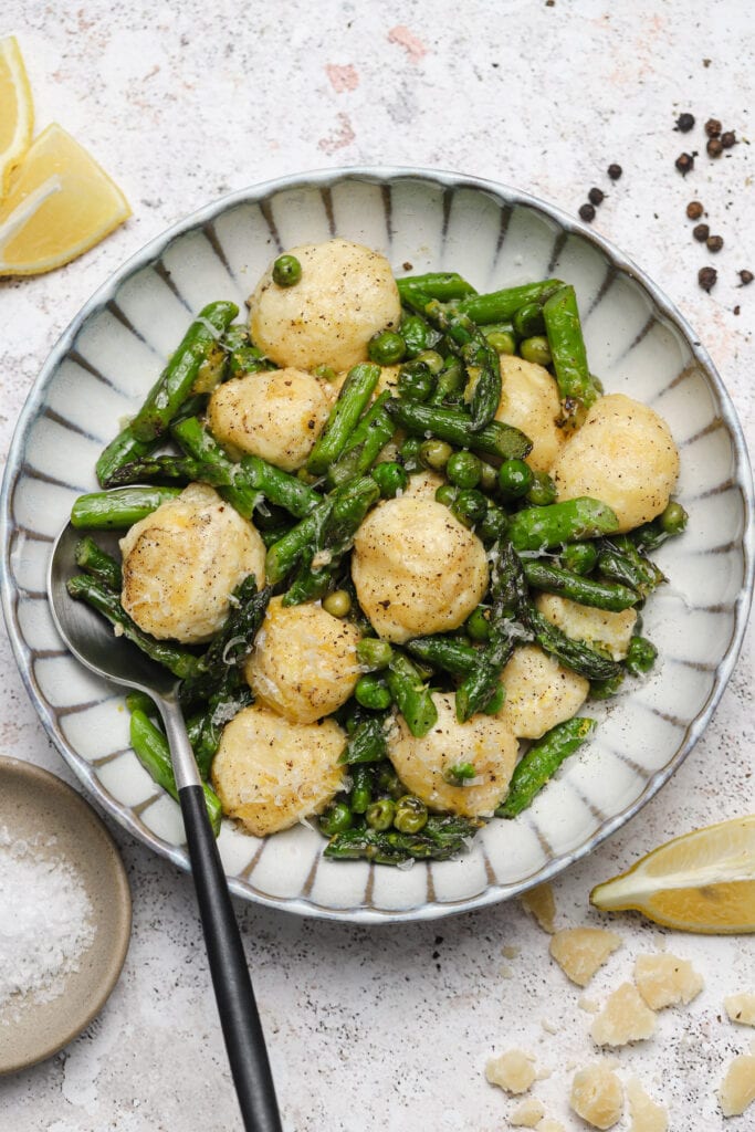 Spring ricotta gnudi with peas and asparagus in a bowl with a spoon.