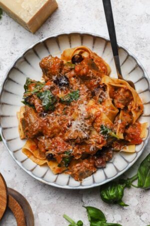 Braised lamb ragu with basil olives and capers in a bowl with fresh pasta.