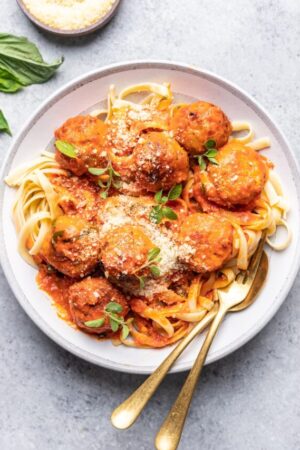 Chicken meatballs over a bowl of pasta with grated Parmesan.