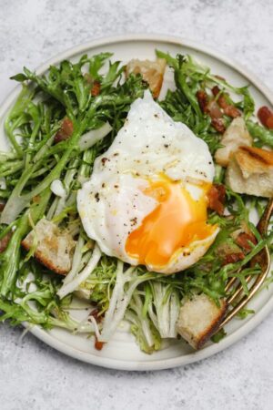 Frisée salad on a plate with homemade croutons and runny egg.