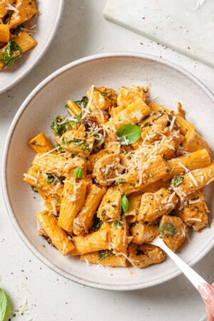 Tuscan chicken pasta with fresh basil and grated Parmesan on plate with fork.