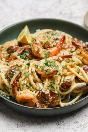 Spicy shrimp and andouille pasta with parsley and lemon wedges.