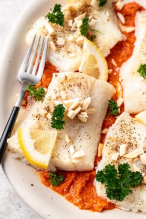 Close up of pan seared cod with romesco sauce on plate.