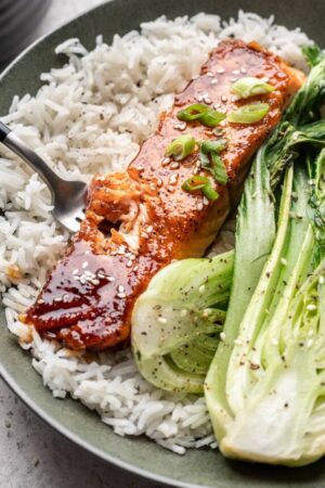 Honey garlic salmon fillet on bed of white rice and side of bokchoy on plate with fork.