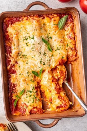 Three cheese manicotti in baking tray with piece removed.