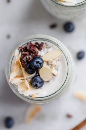 overnight oats recipe in a glass container with blueberries cocoa nibs and sliced almonds.