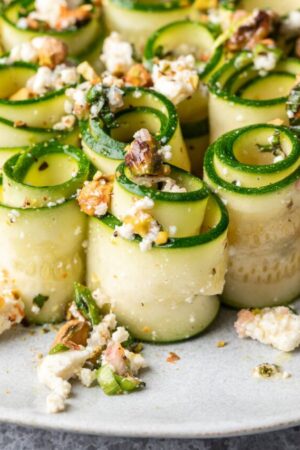 Raw zucchini rolled into semi-twists on plate and dressed with salad on top.