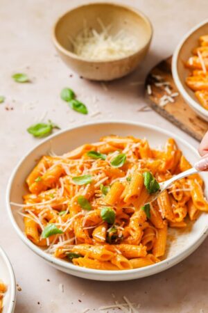 Hand scooping vodka sauce pasta with spoon.