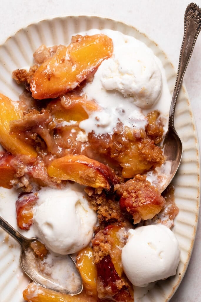 Close up of peach crumble with vanilla ice cream on a plate with spoons.