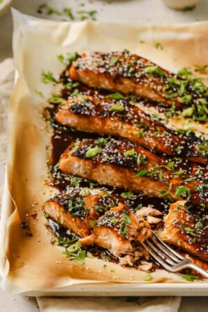 Close up of fork cutting honey sriracha salmon fillets garnished with herbs.