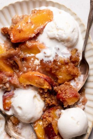 Close up of peach crumble with vanilla ice cream on a plate with spoons.
