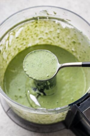 Spoon of green goddess salad dressing above food processor.