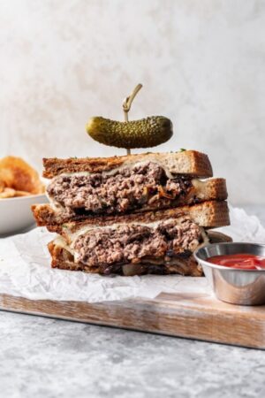 Stacked and sliced patty melt held by toothpick with pickle on top.