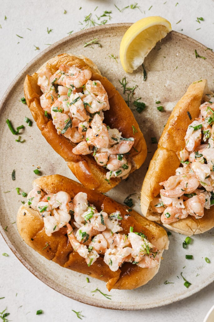 Three warm Connecticut style shrimp rolls on a plate with fresh tarragon.