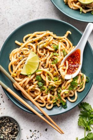 Chili ginger noodles on green plate and spoon of red chili sauce.